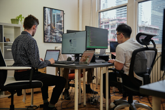 Deux membres de l'équipe de Nimbus Learning sont assis l'un à côté de l'autre, travaillant d'arrache-pied sur leur ordinateur.