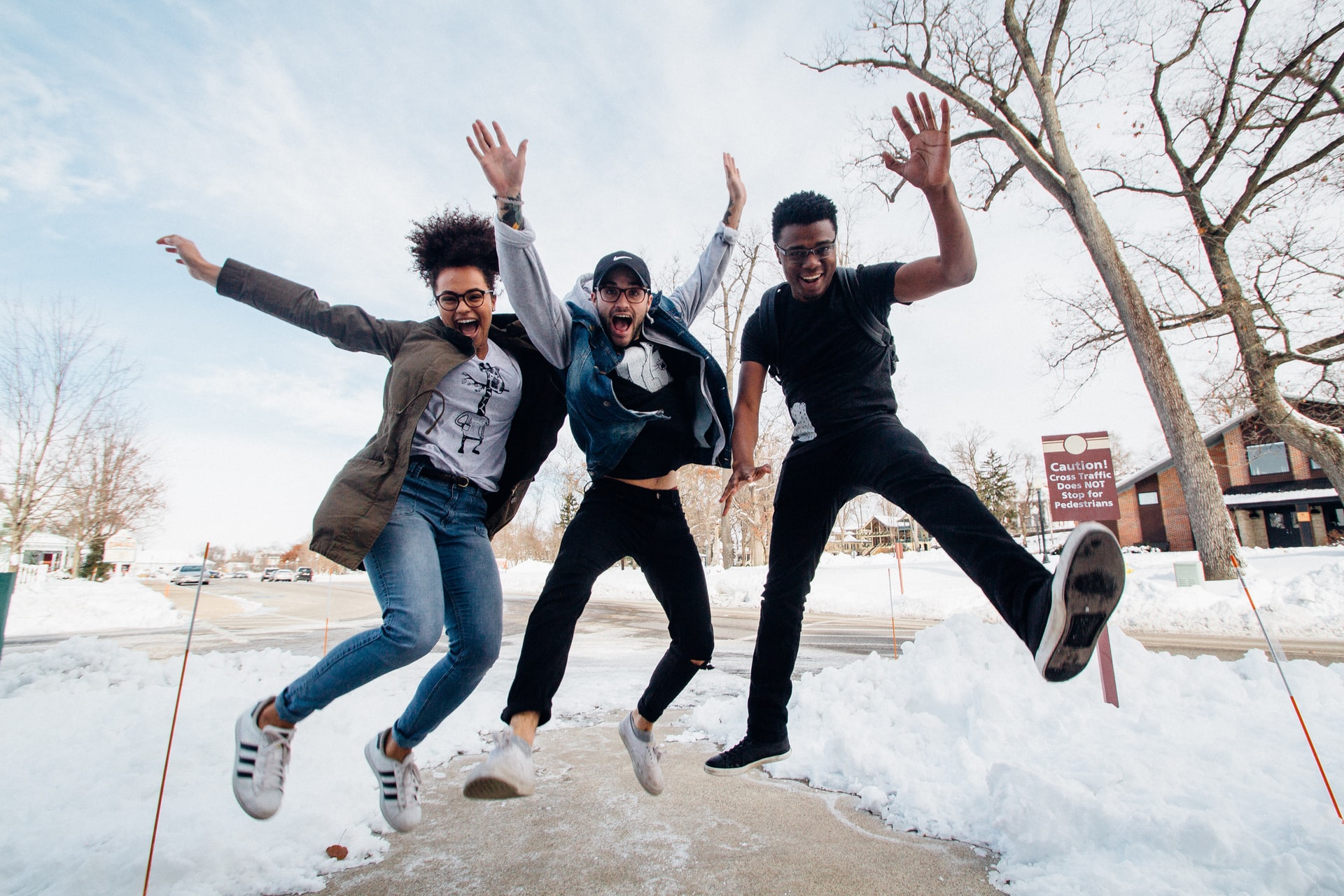 Three friends who met through a mentorship program in efforts to rebuild the in person campus community jump in celebration. The are standing on a sidewalk flanked by snow piles.