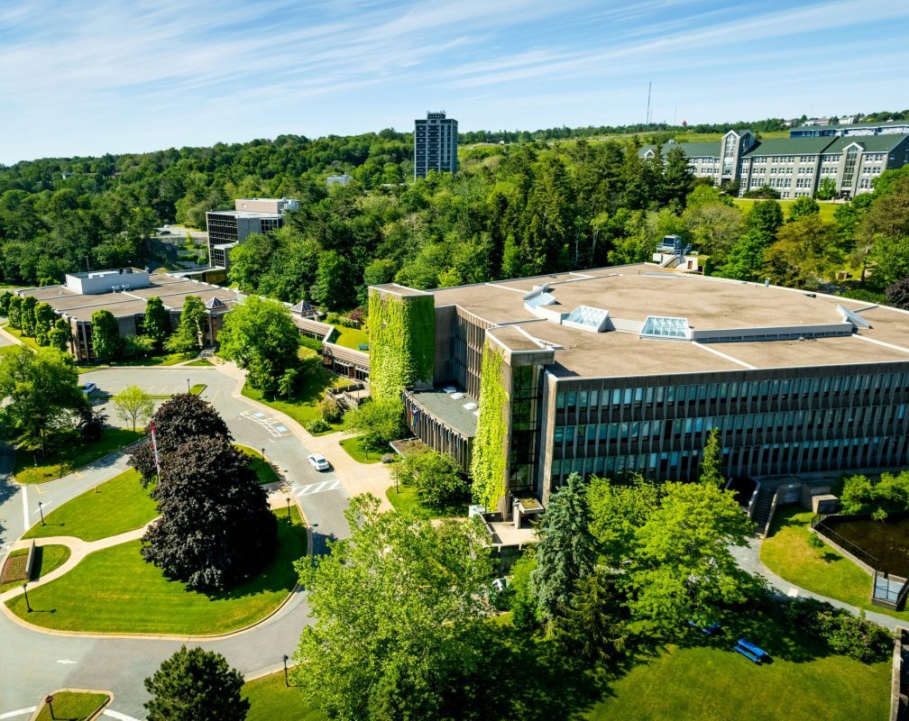 An areal view of a brown building with a flat roof sitting on a campus full of trees