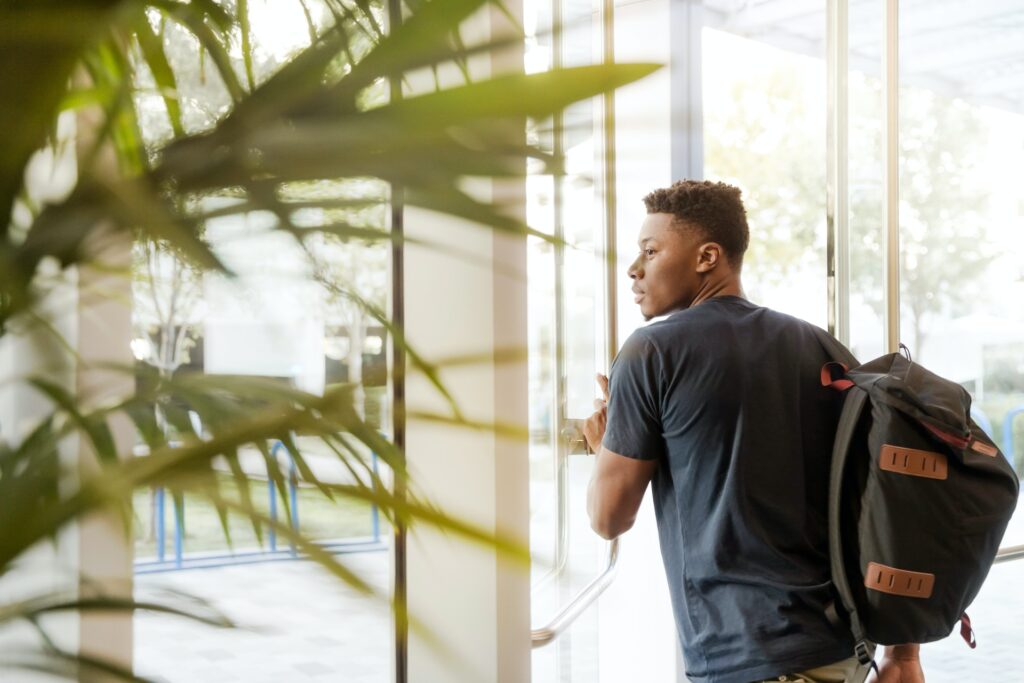 Man holding backpack walking through a door, improve student success find tutors